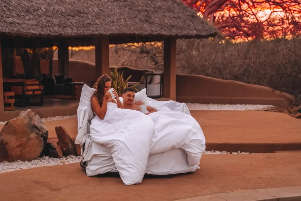Couple enjoying a romantic outdoor bed experience at a luxury safari lodge during sunset in Tanzania