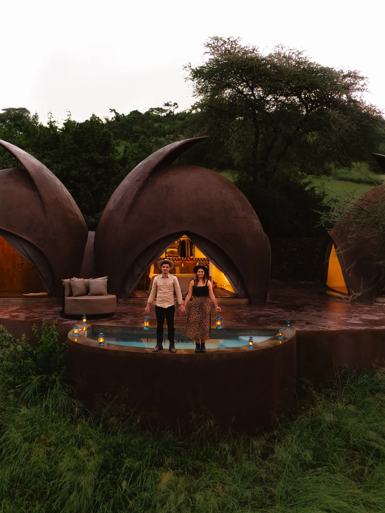 Couple with lanterns by a plunge pool outside sculpted dome suites at dusk, Serengeti, Tanzania