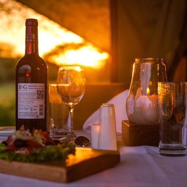 Candlelit dinner table with wine and a sunset view on a safari deck, Serengeti, Tanzania