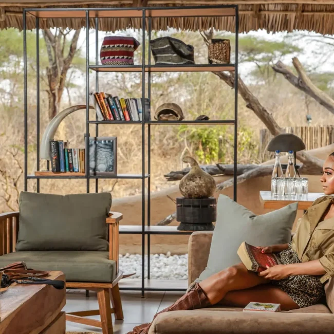 Guest relaxing with a book in the lounge of a luxury safari camp overlooking the bush, Tanzania