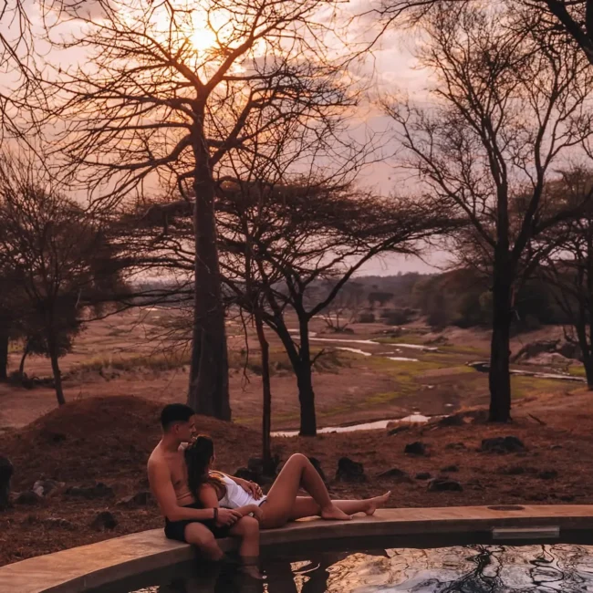 Couple relaxing by a private plunge pool at sunset overlooking a river valley, Serengeti, Tanzania